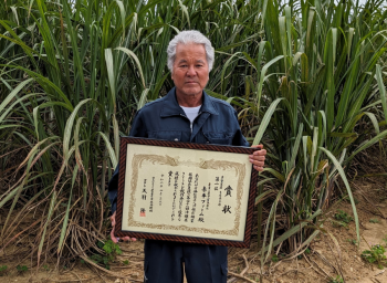 <赤平ファーム玉城さん、さとうきびを背景に>